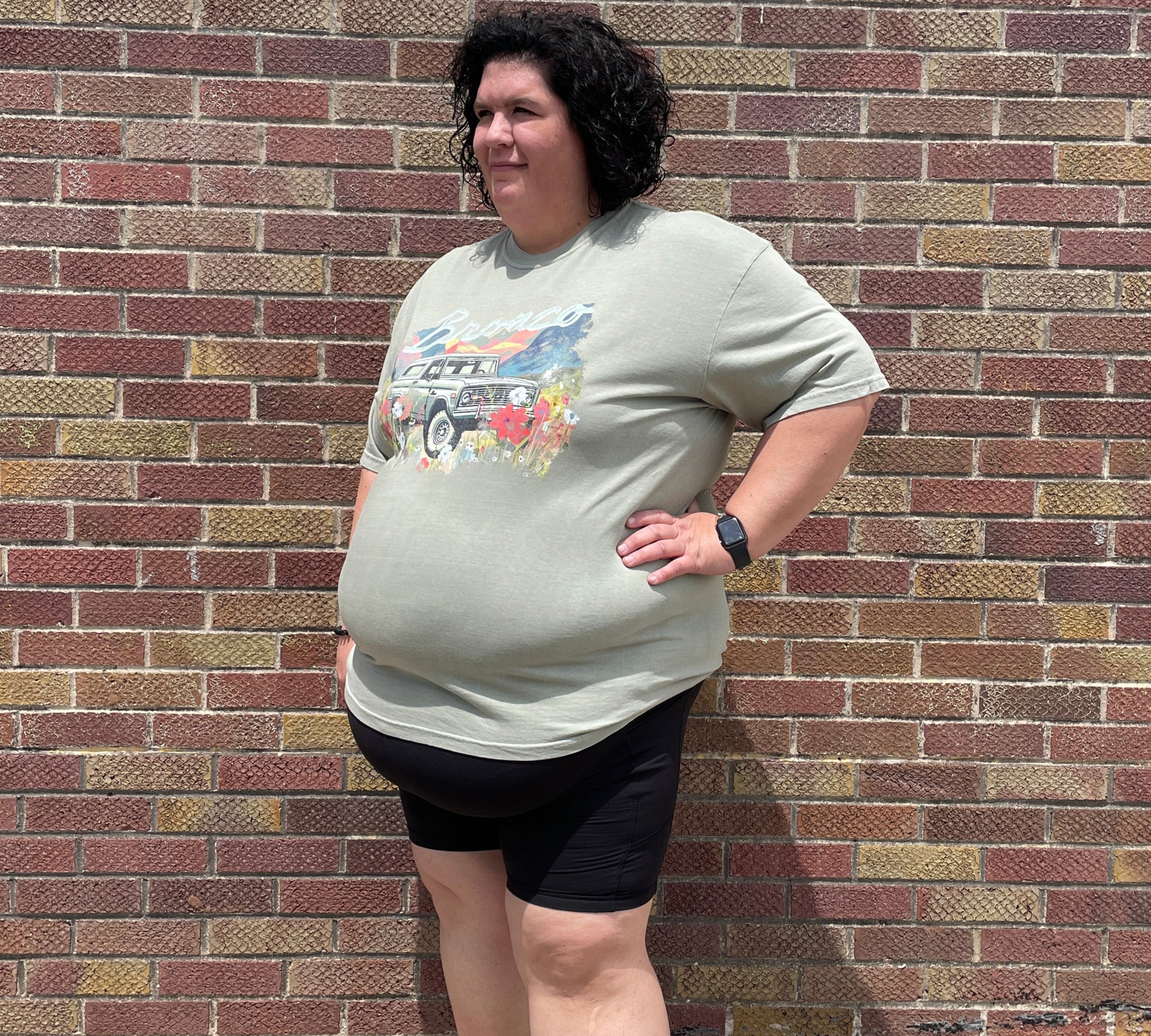 Person standing on a brick sidewalk wearing a light-colored t-shirt with graphics and dark shorts.