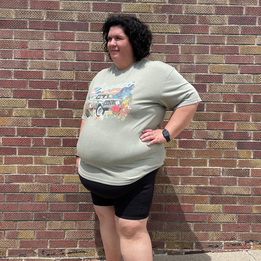 Person standing on a brick sidewalk wearing a light-colored t-shirt with graphics and dark shorts.